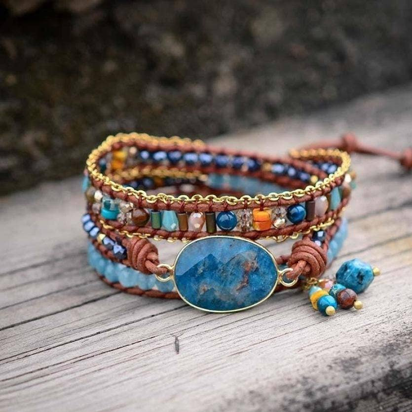 Multicolored beaded bracelet with a large blue stone on a wooden surface, labeled 'Free Spirit Shop'.