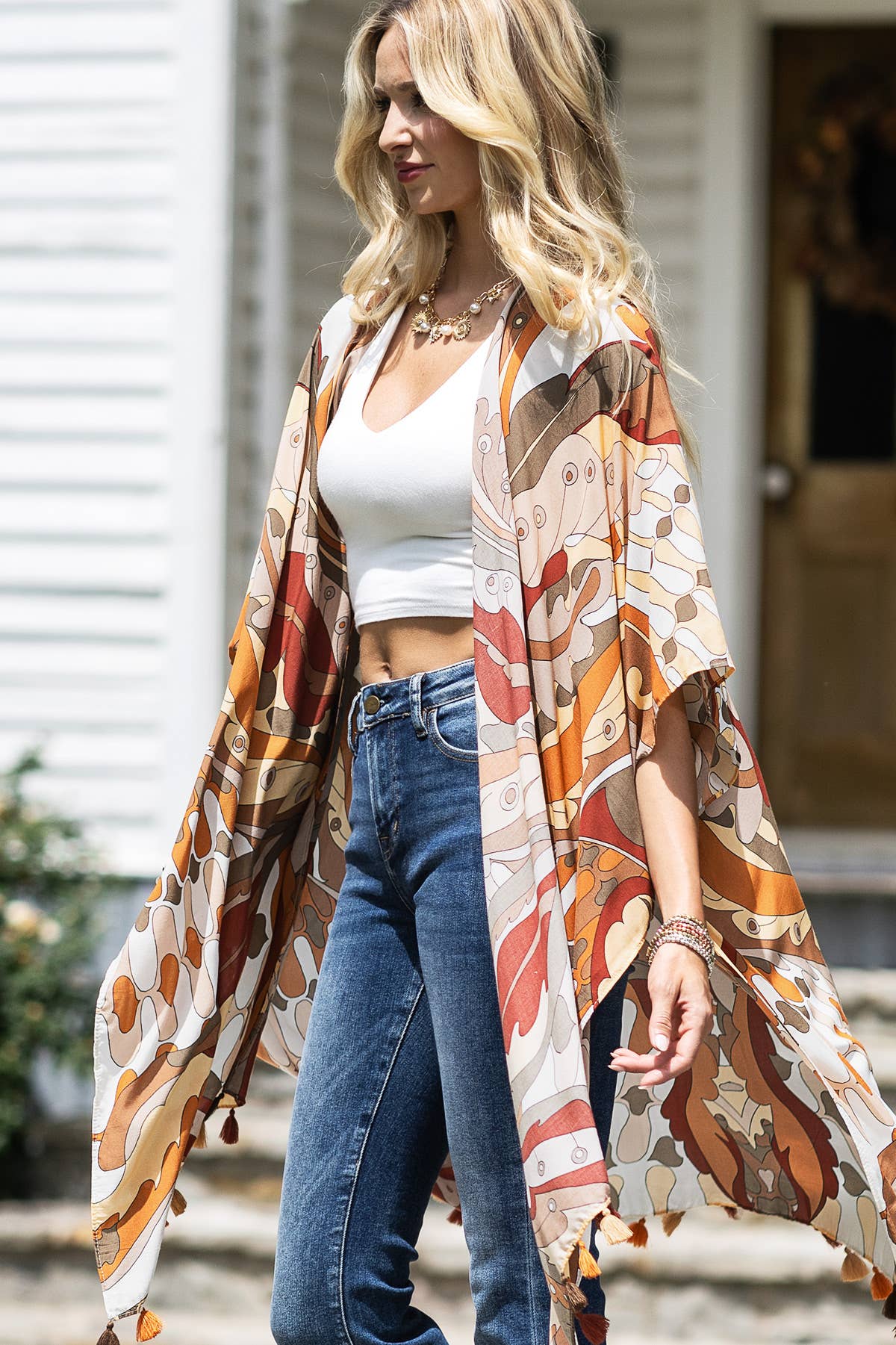 Woman wearing a patterned kimono over a white top and blue jeans outdoors.