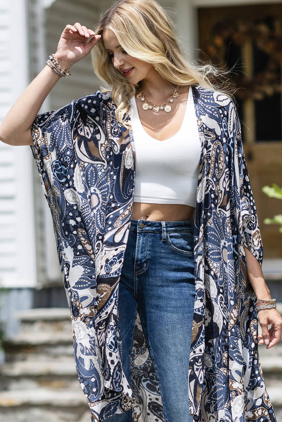 Woman wearing a patterned kimono over a white top and blue jeans, standing outdoors.