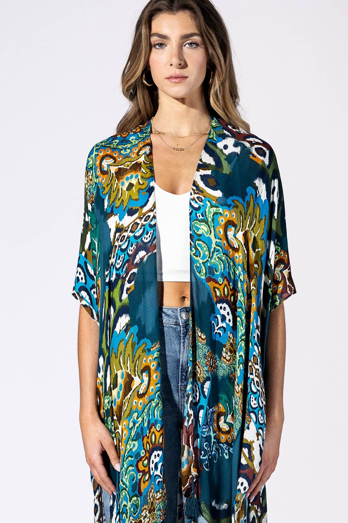 Woman wearing a colorful patterned kimono over a white top and jeans on a white background