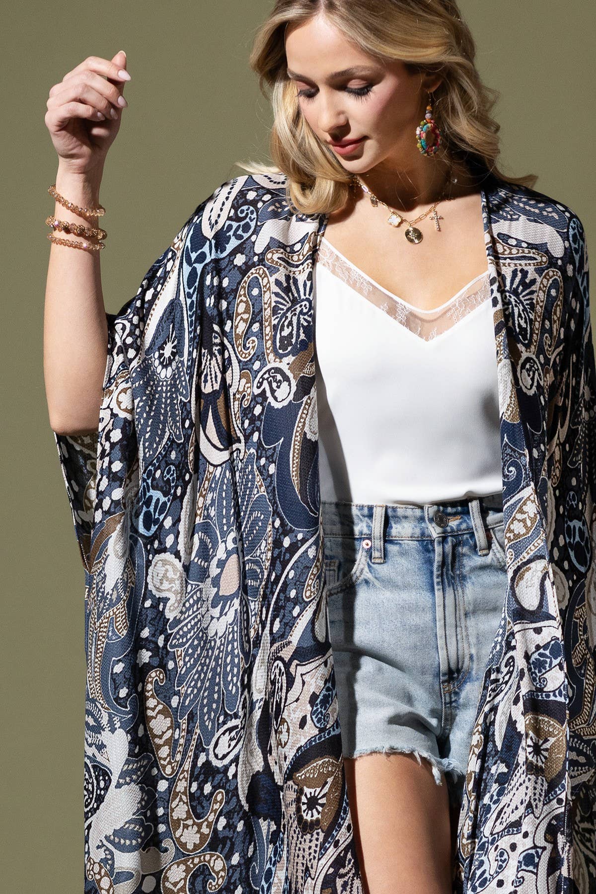 Woman wearing a patterned kimono over a white top and denim shorts on a neutral background
