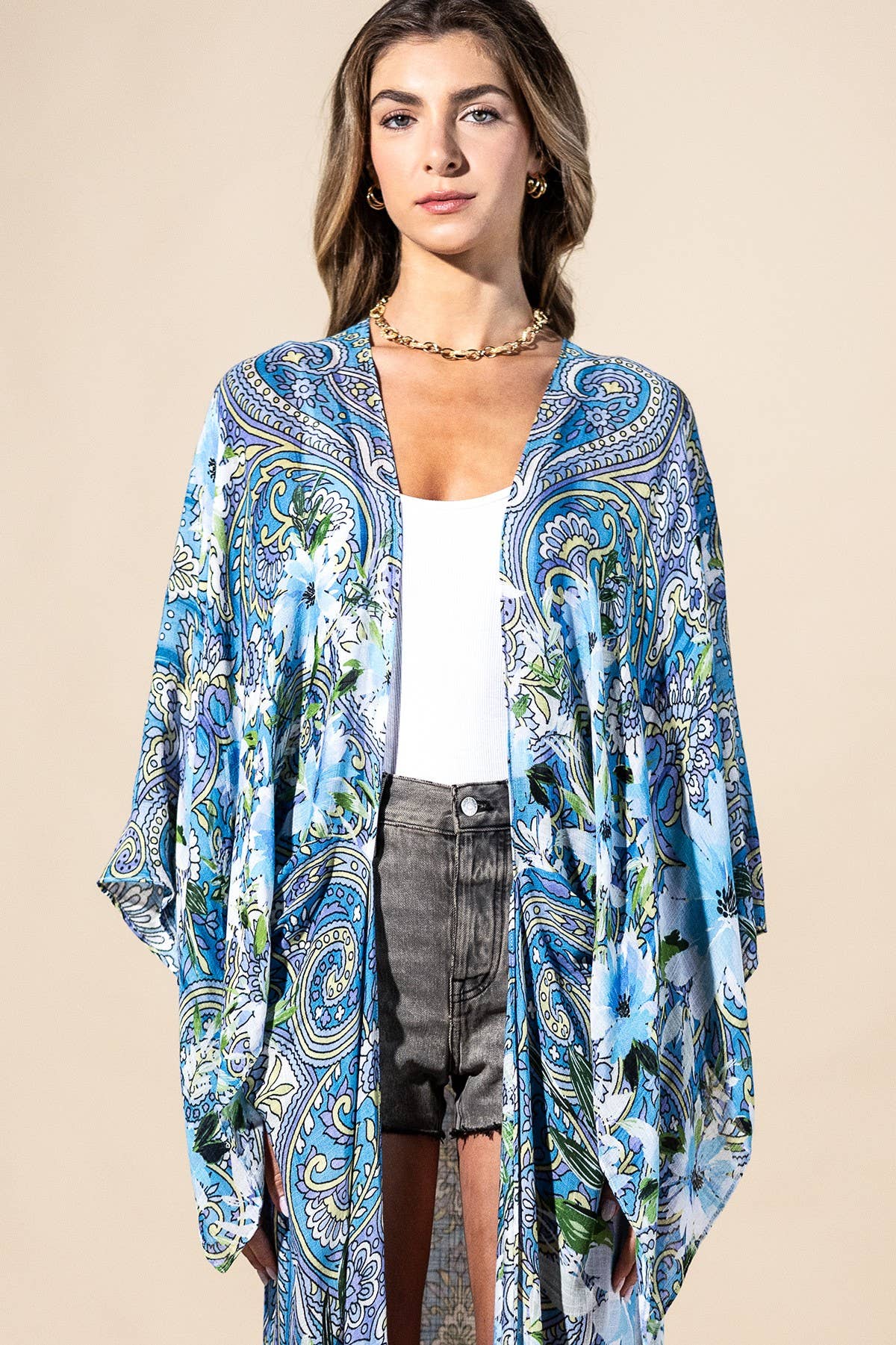Woman wearing a blue patterned kimono over a white top and gray shorts on a beige background
