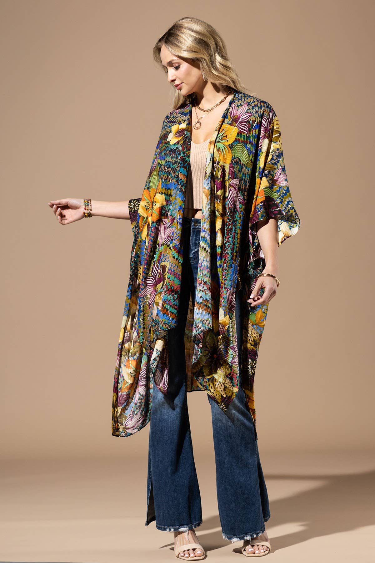 Woman wearing a colorful floral kimono over a beige top and blue pants on a beige background