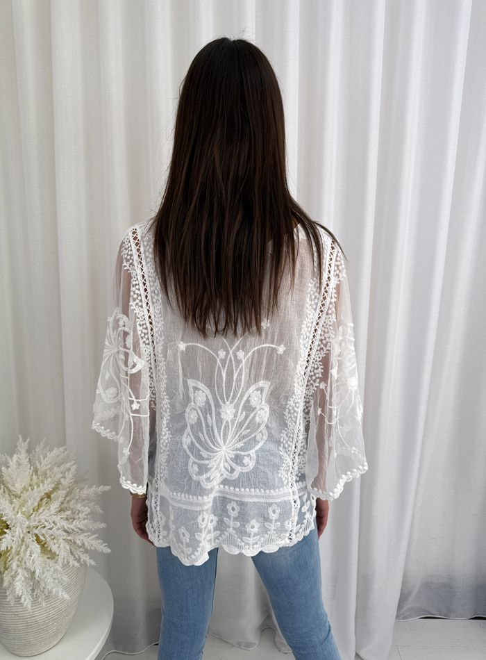 Person wearing a white lace top with floral patterns against a white curtain background