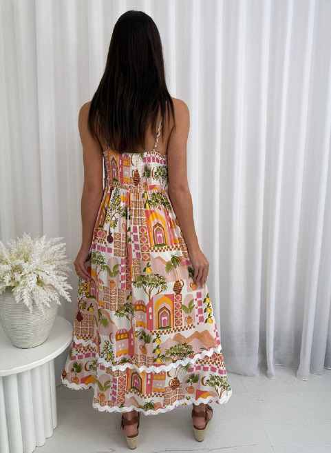 Woman wearing a colorful dress with a pattern of houses and trees, standing in front of white curtains.