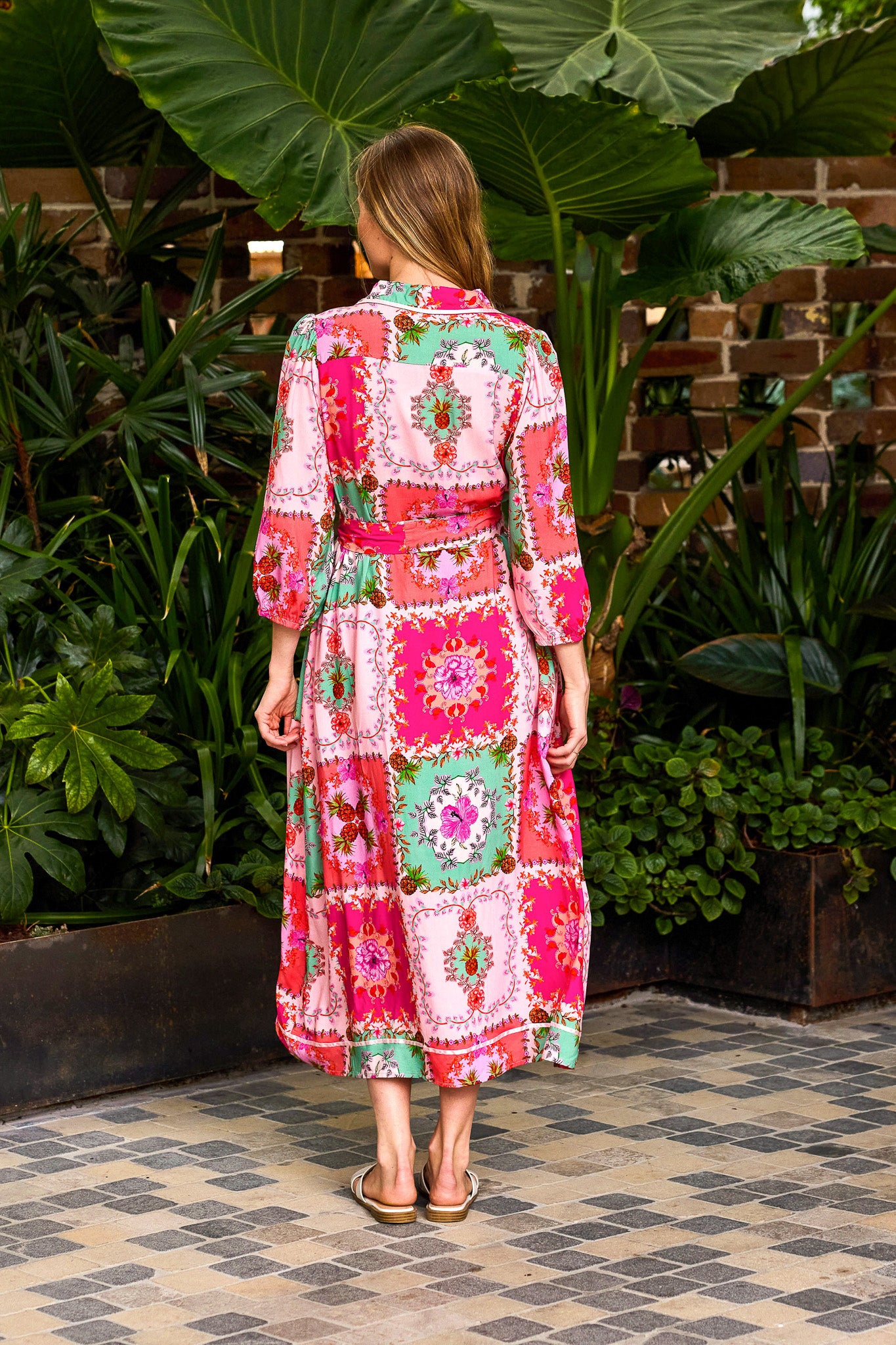 Woman wearing a colorful patterned dress standing in a garden setting.