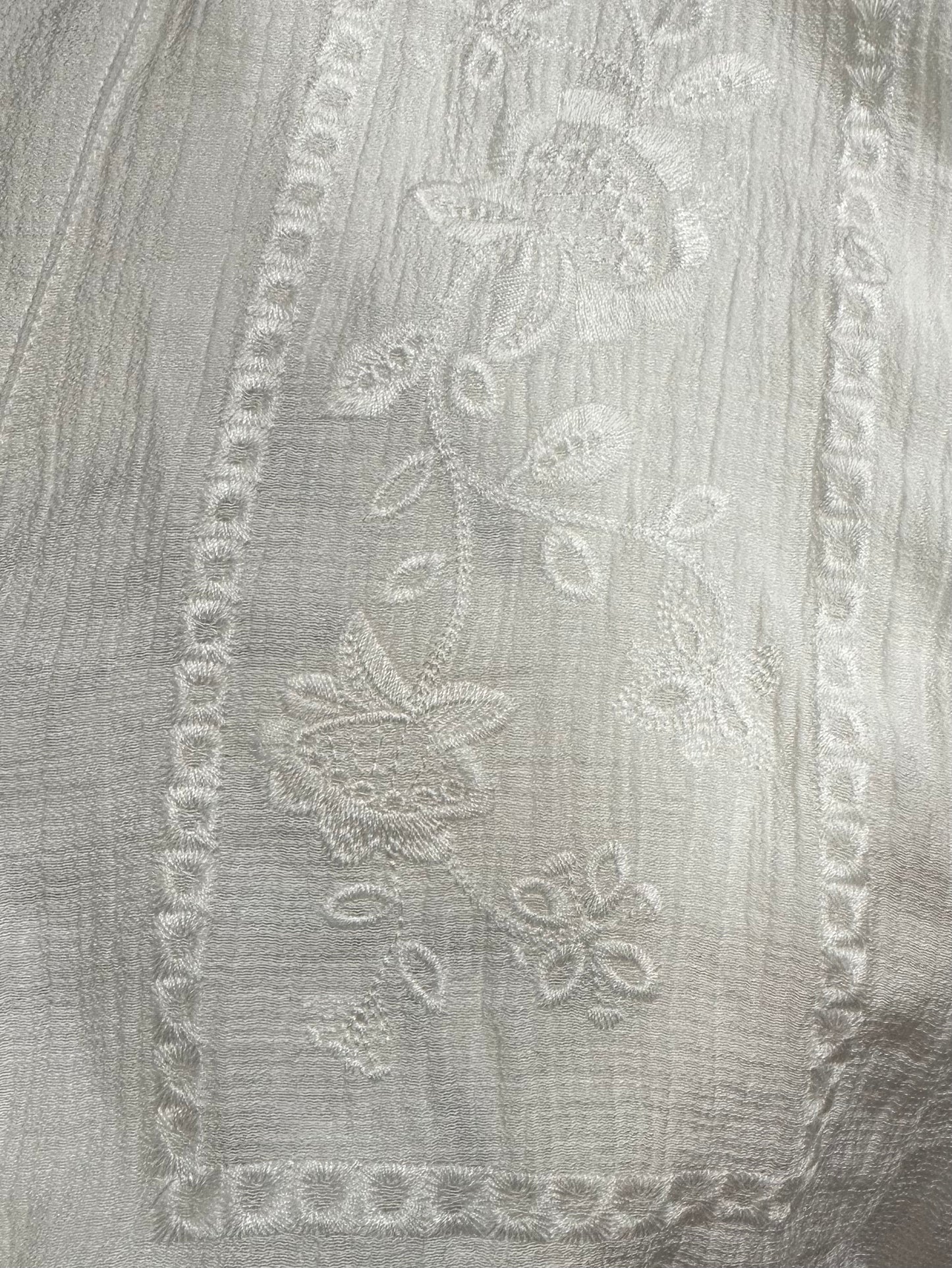 Close-up of a white embroidered fabric with floral and geometric patterns on a textured background.