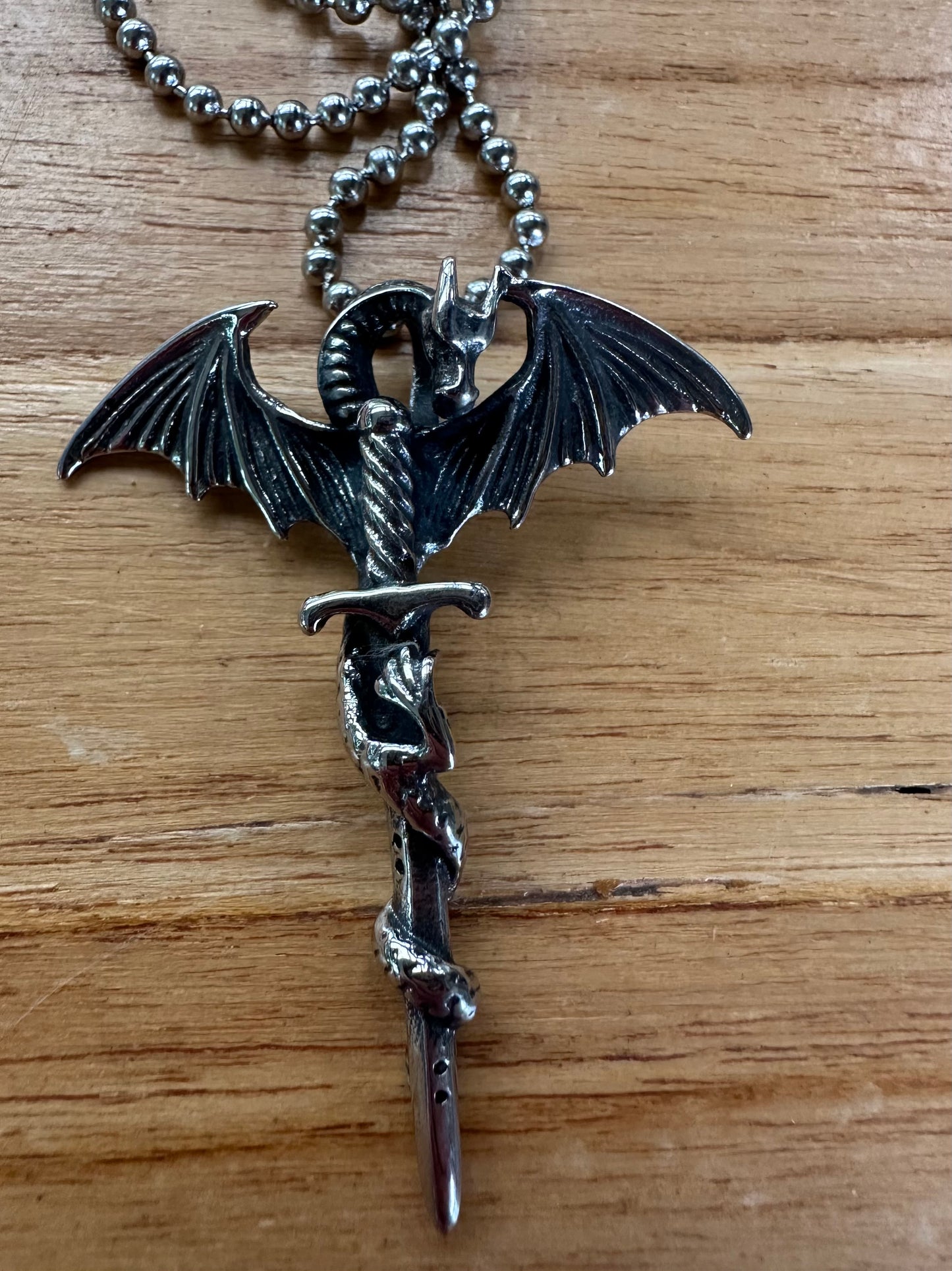 Silver dragon pendant on a chain against a wooden background