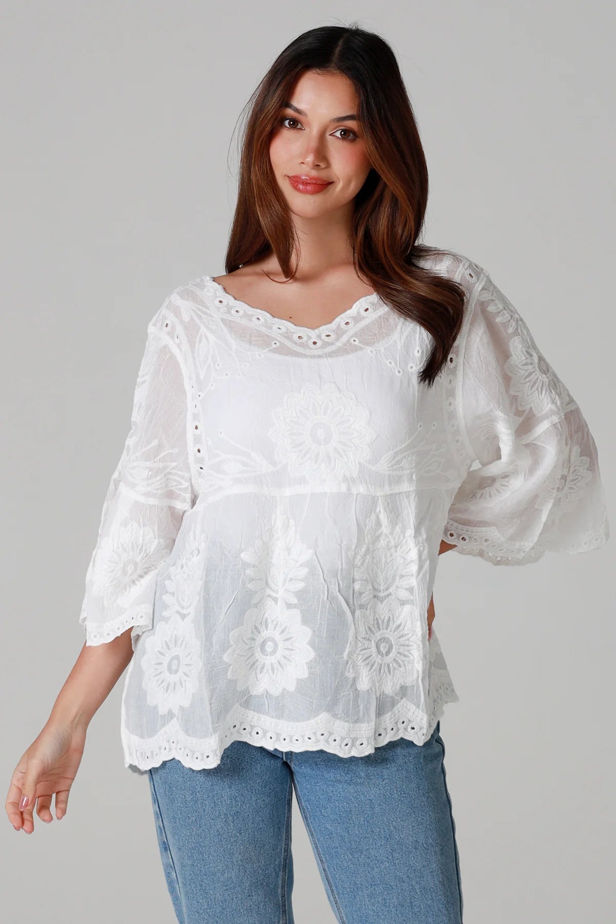 Woman wearing a white lace top with blue jeans on a gray background