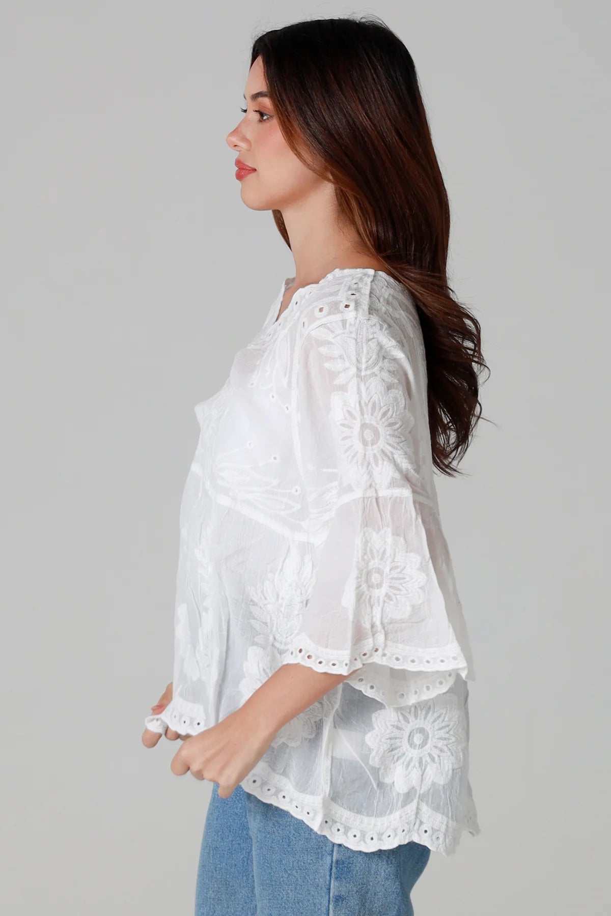 Woman wearing a white lace top and blue jeans on a gray background