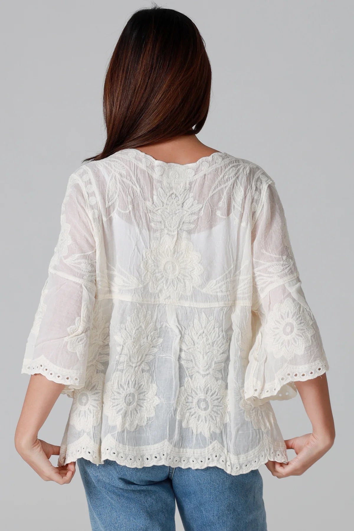 Woman wearing a white lace blouse with blue jeans on a gray background