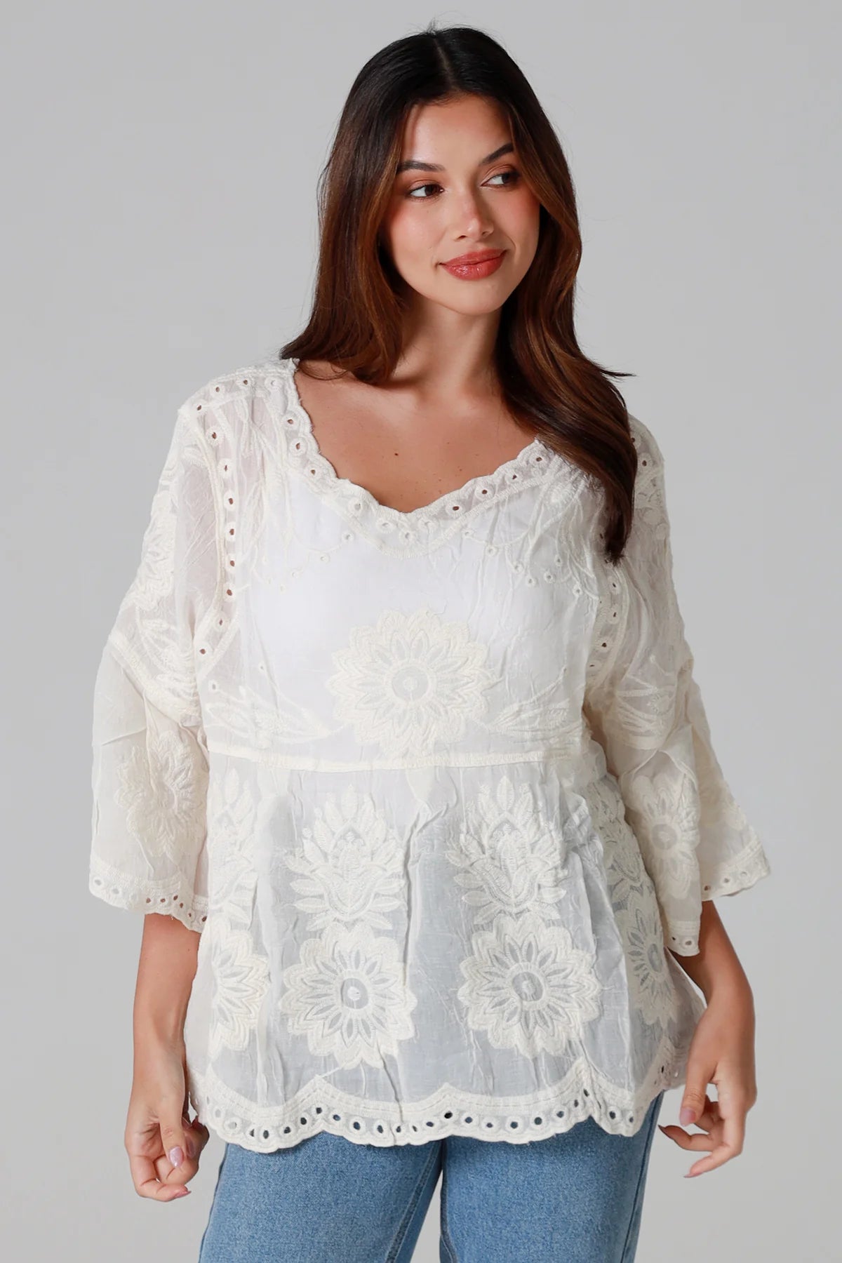 Woman wearing a white lace top with blue jeans on a gray background