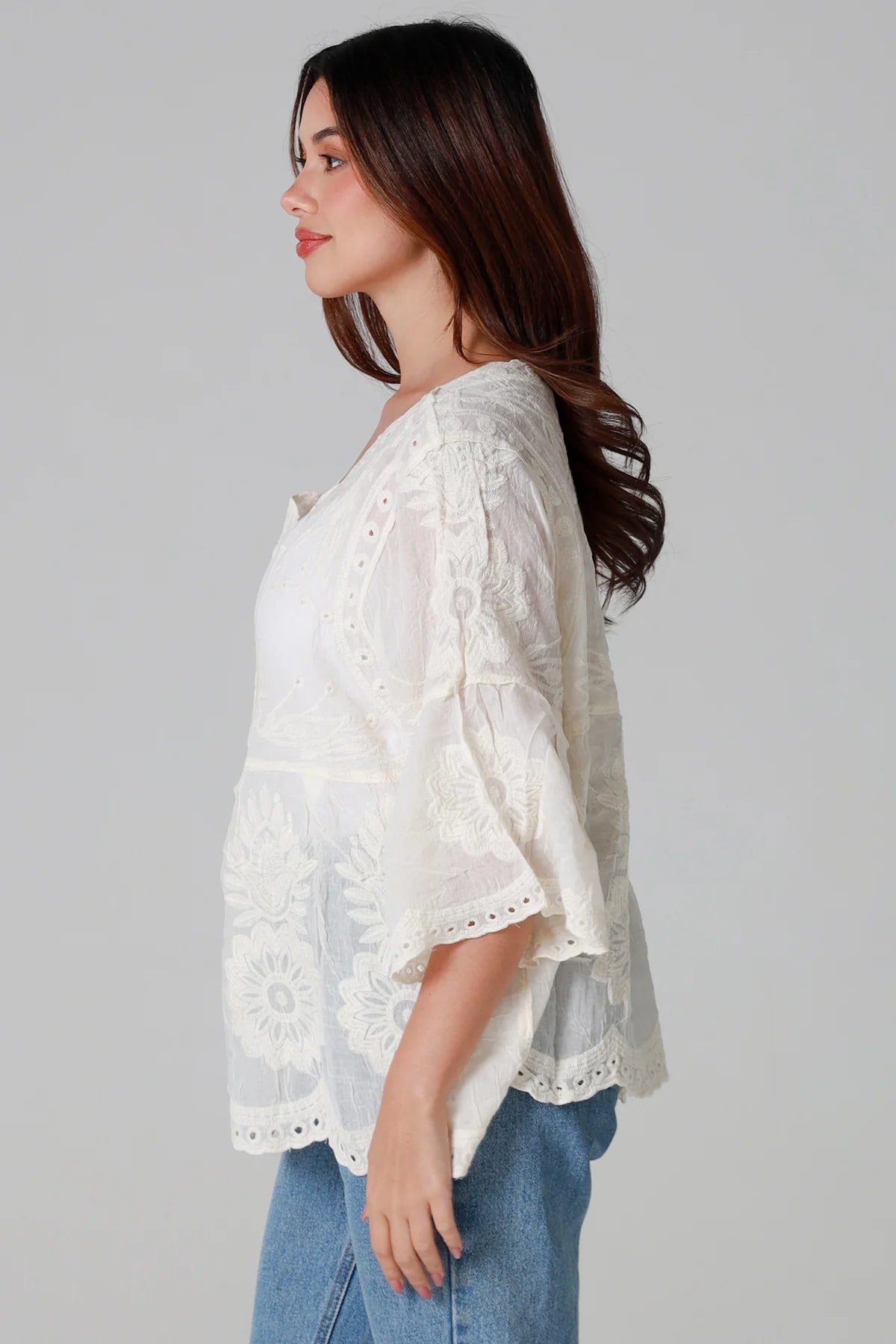 Woman wearing a white lace top and blue jeans on a gray background