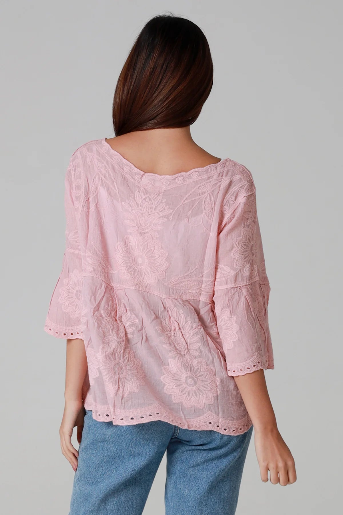 Person wearing a pink lace top and blue jeans on a gray background