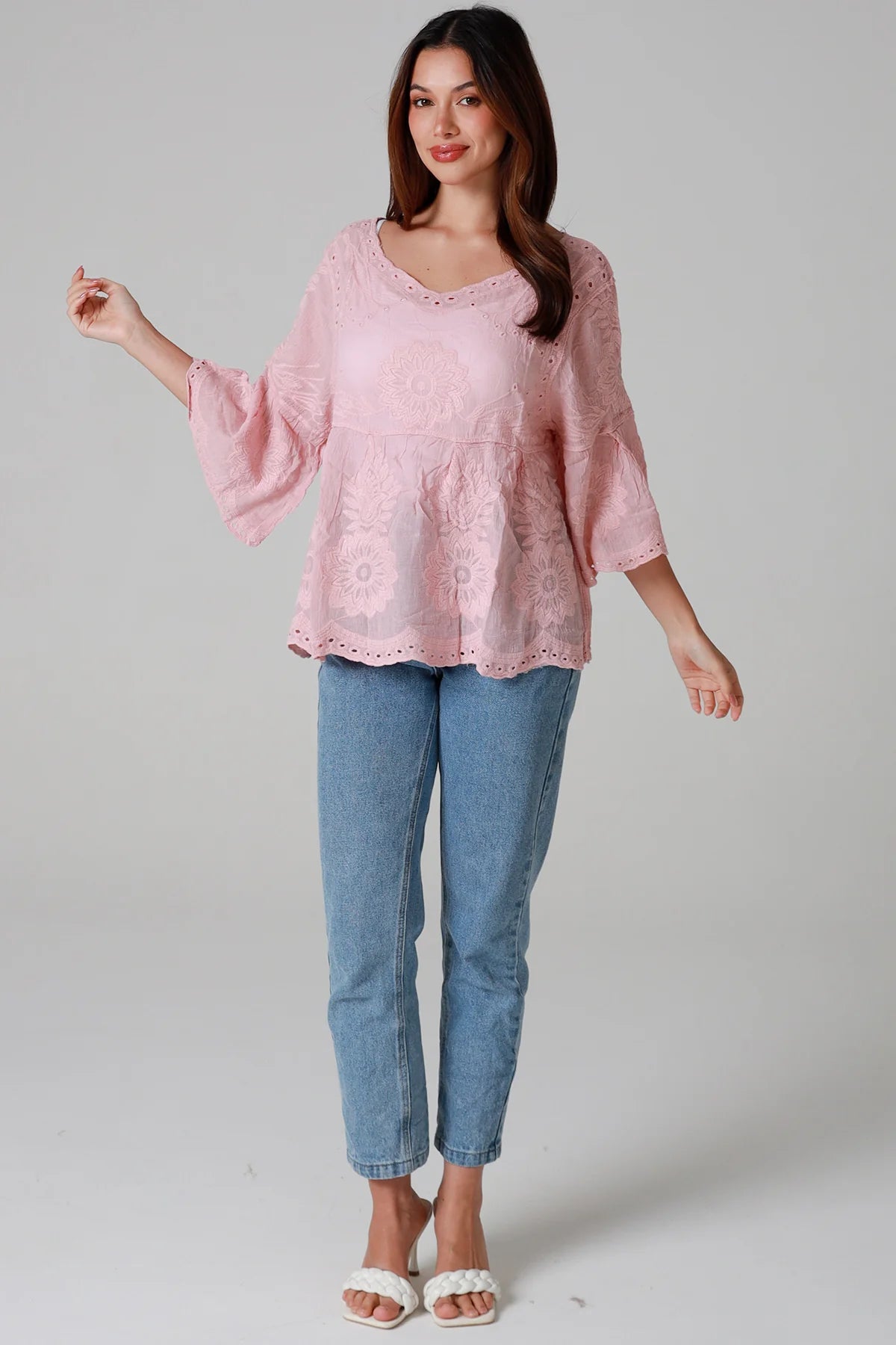 Woman wearing a pink blouse and blue jeans on a plain background