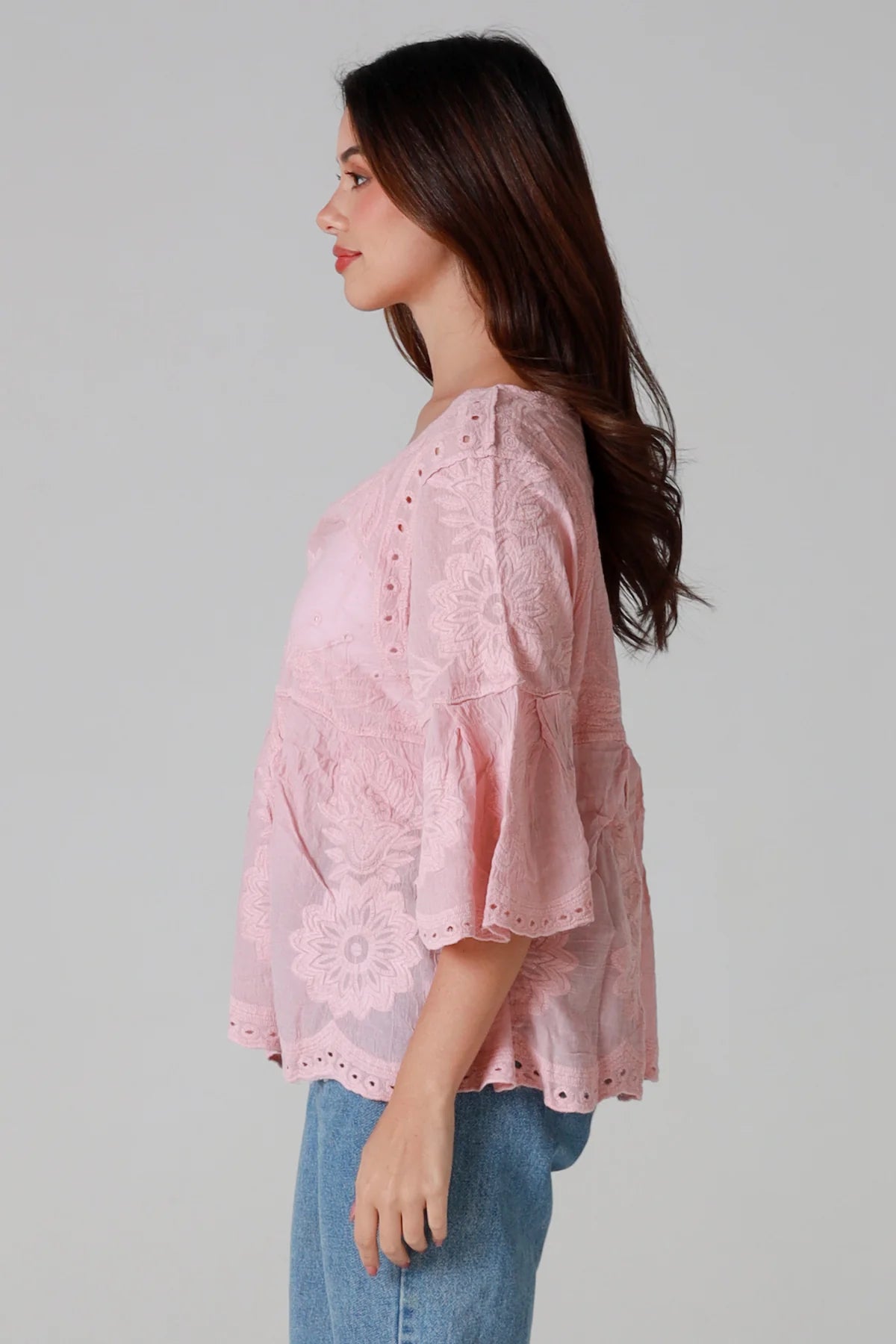 Woman wearing a pink lace top and blue jeans on a gray background