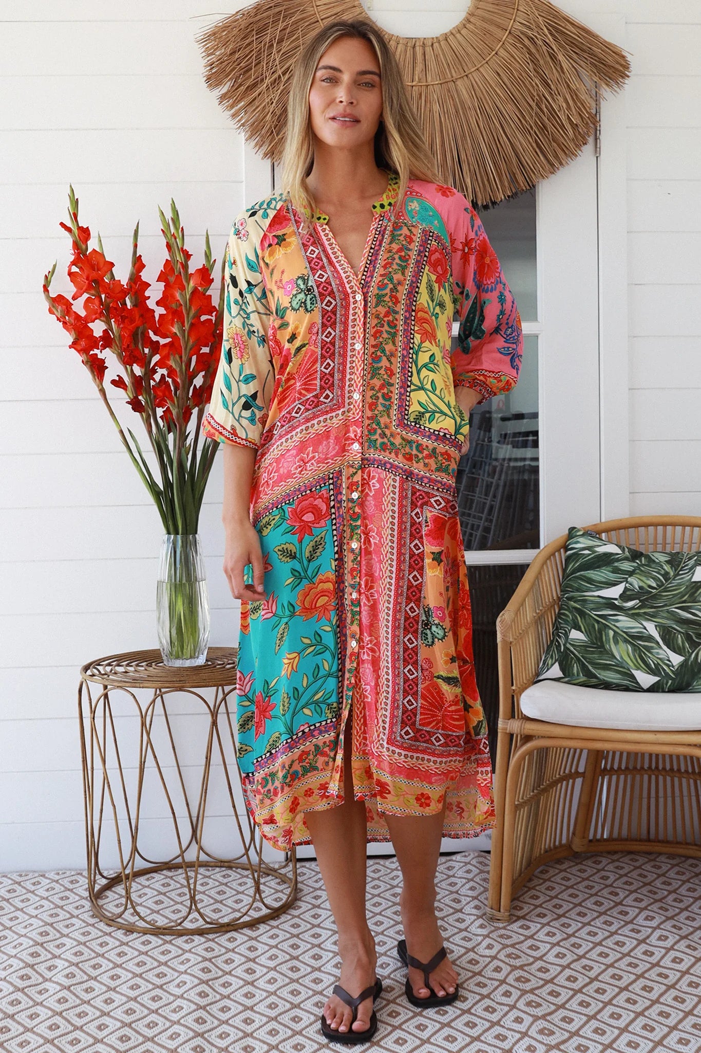 Woman wearing a colorful patterned dress standing in a home setting with decorative elements.