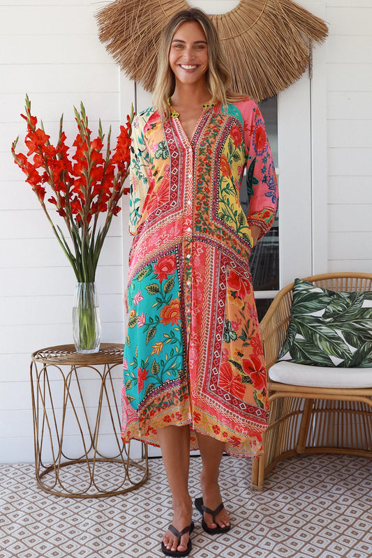 Woman wearing a colorful dress with a decorative hat and floral arrangement in a home setting.