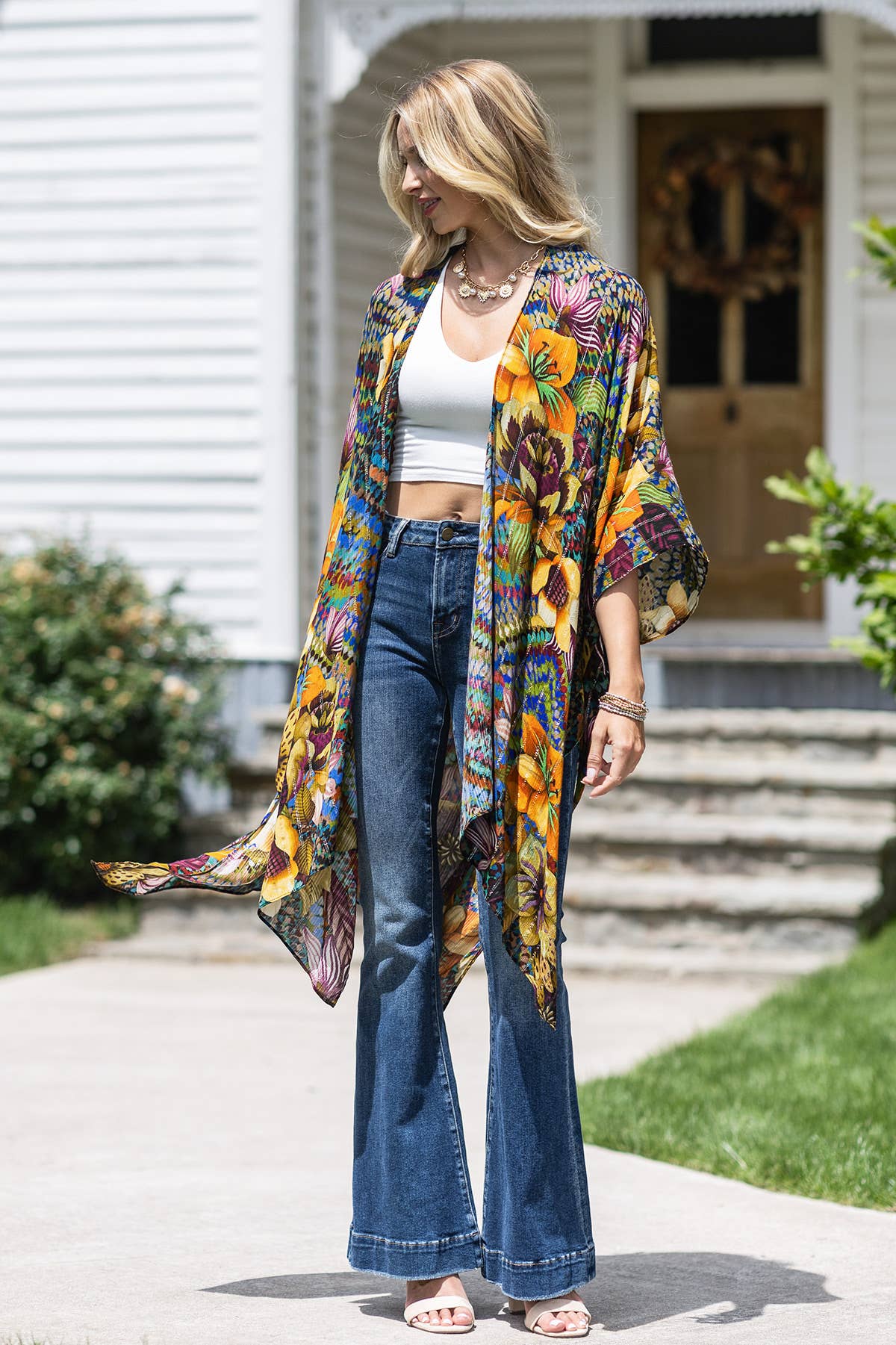 Woman wearing a colorful floral kimono over a white top and blue jeans, standing on a sidewalk.