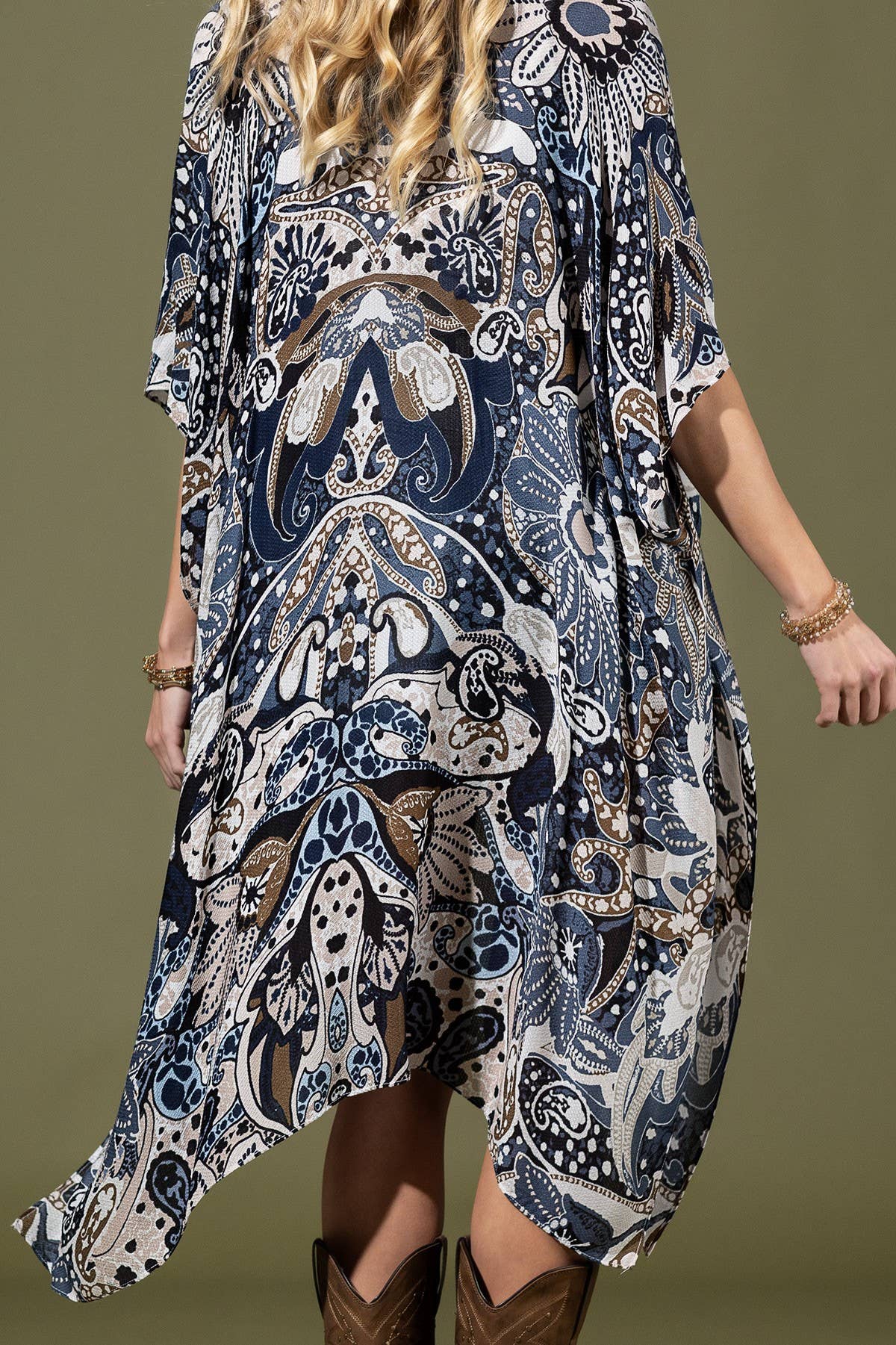 Woman wearing a patterned dress with boots on a plain background