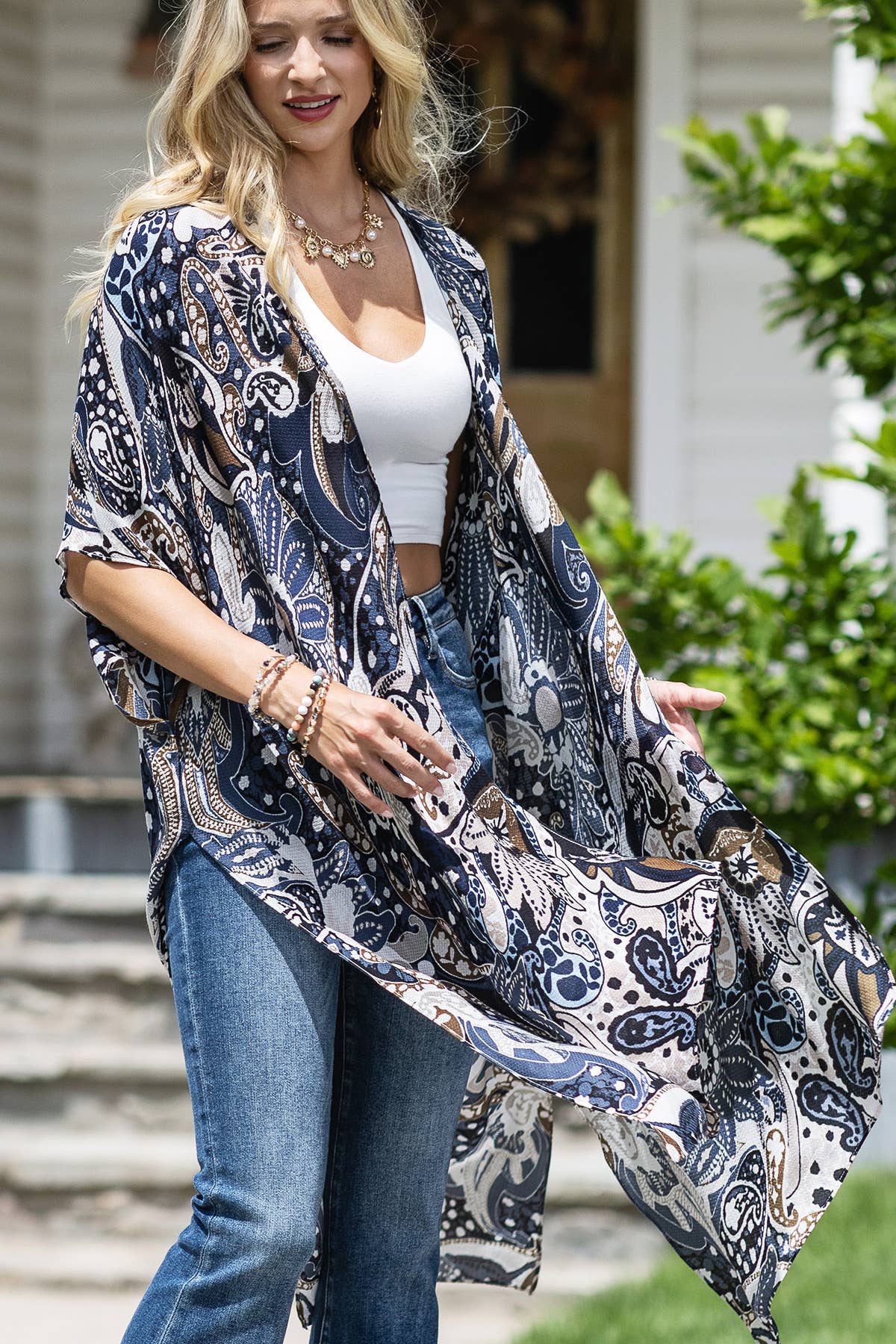 Woman wearing a patterned kimono over a white top and jeans outdoors.