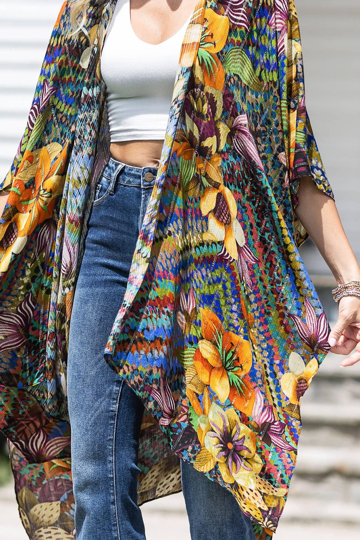 Person wearing a colorful floral kimono over a white crop top and blue jeans.