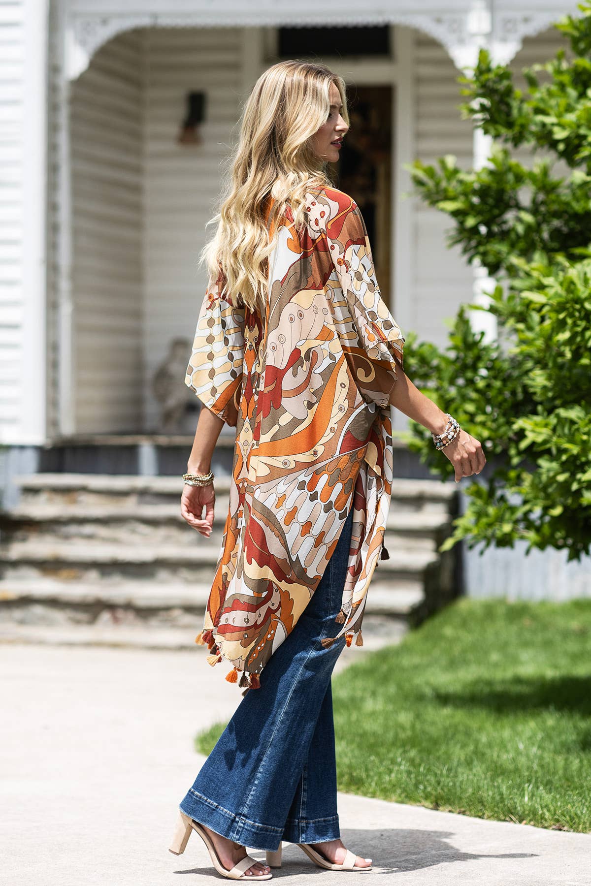Woman wearing a patterned dress and blue jeans standing outdoors.