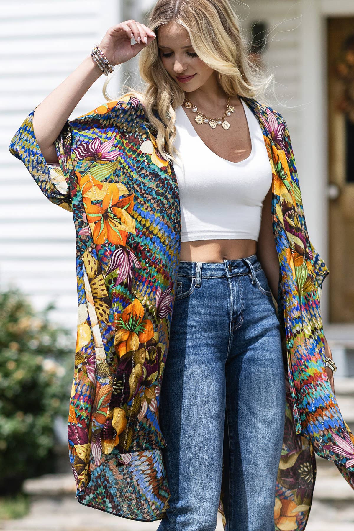 Woman wearing a colorful floral kimono over a white crop top and blue jeans.