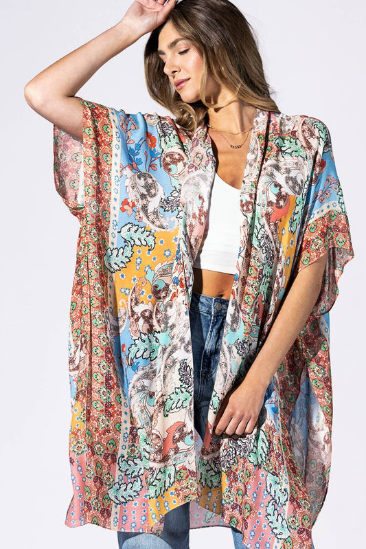 Woman wearing a colorful patterned kimono over a white top and jeans on a white background