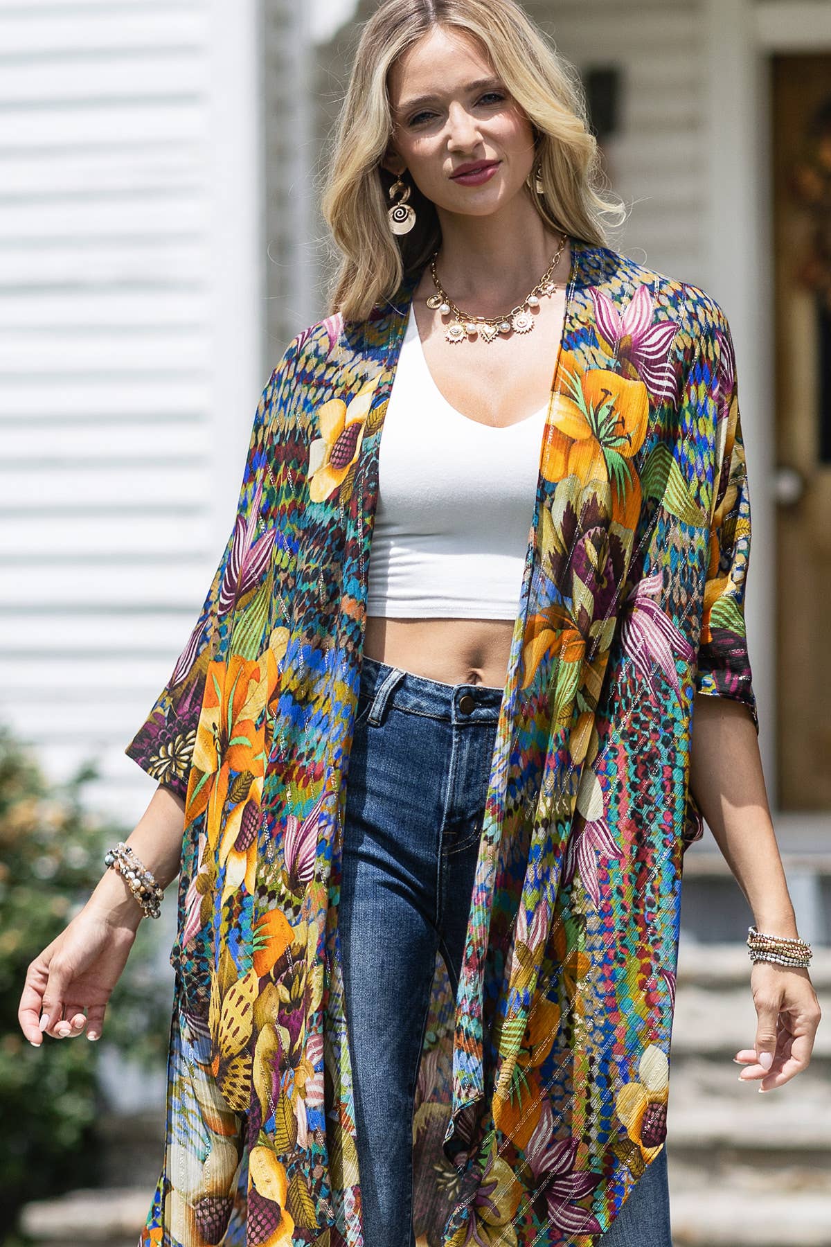 Woman wearing a colorful kimono-style jacket with a white top and blue jeans outdoors.