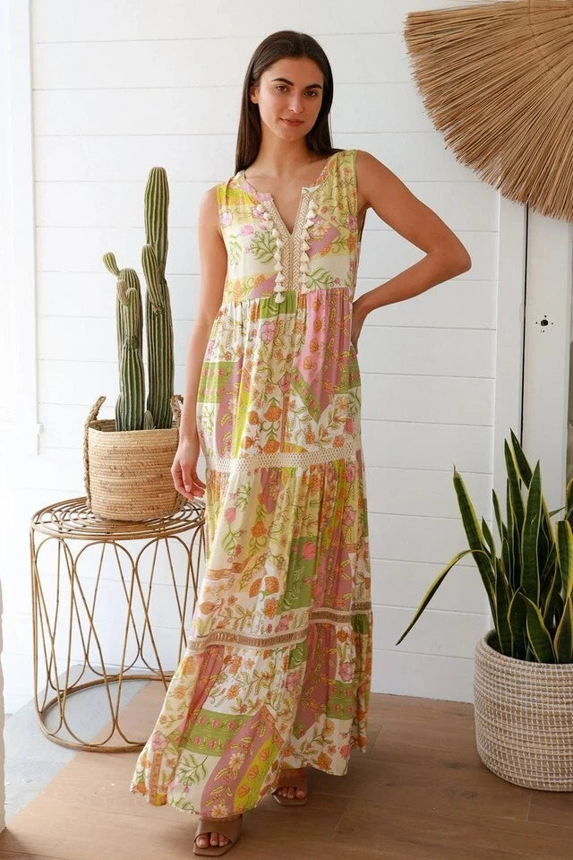 Woman wearing a floral dress standing in a room with plants and a white wall.