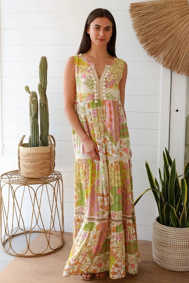 Woman wearing a floral dress standing in a room with plants and a white wall.