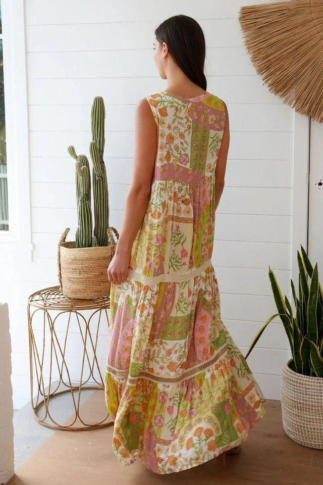 Woman wearing a colorful patchwork dress standing in a room with plants and a white wall.
