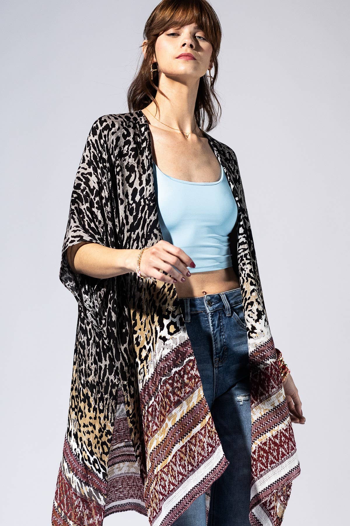 Woman wearing a leopard print and patterned cardigan over a light blue top and jeans on a white background