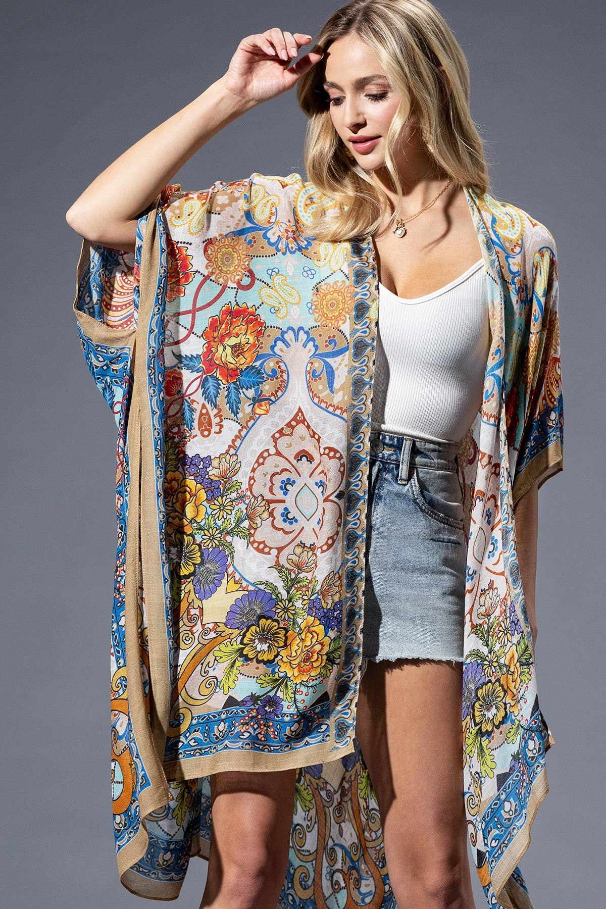 Woman wearing a colorful floral kimono over a white top and denim shorts on a gray background