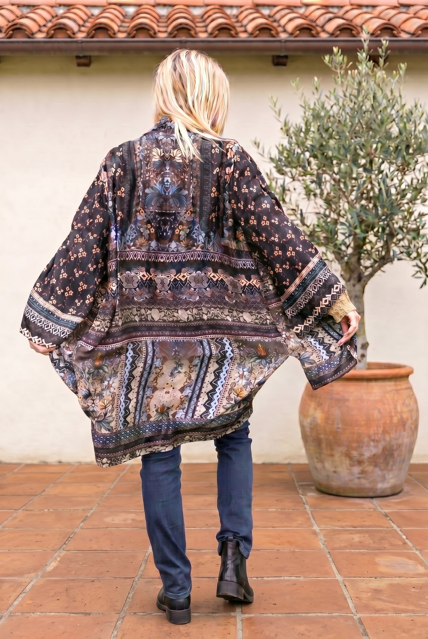 Person wearing a patterned kimono standing outdoors next to a potted plant.