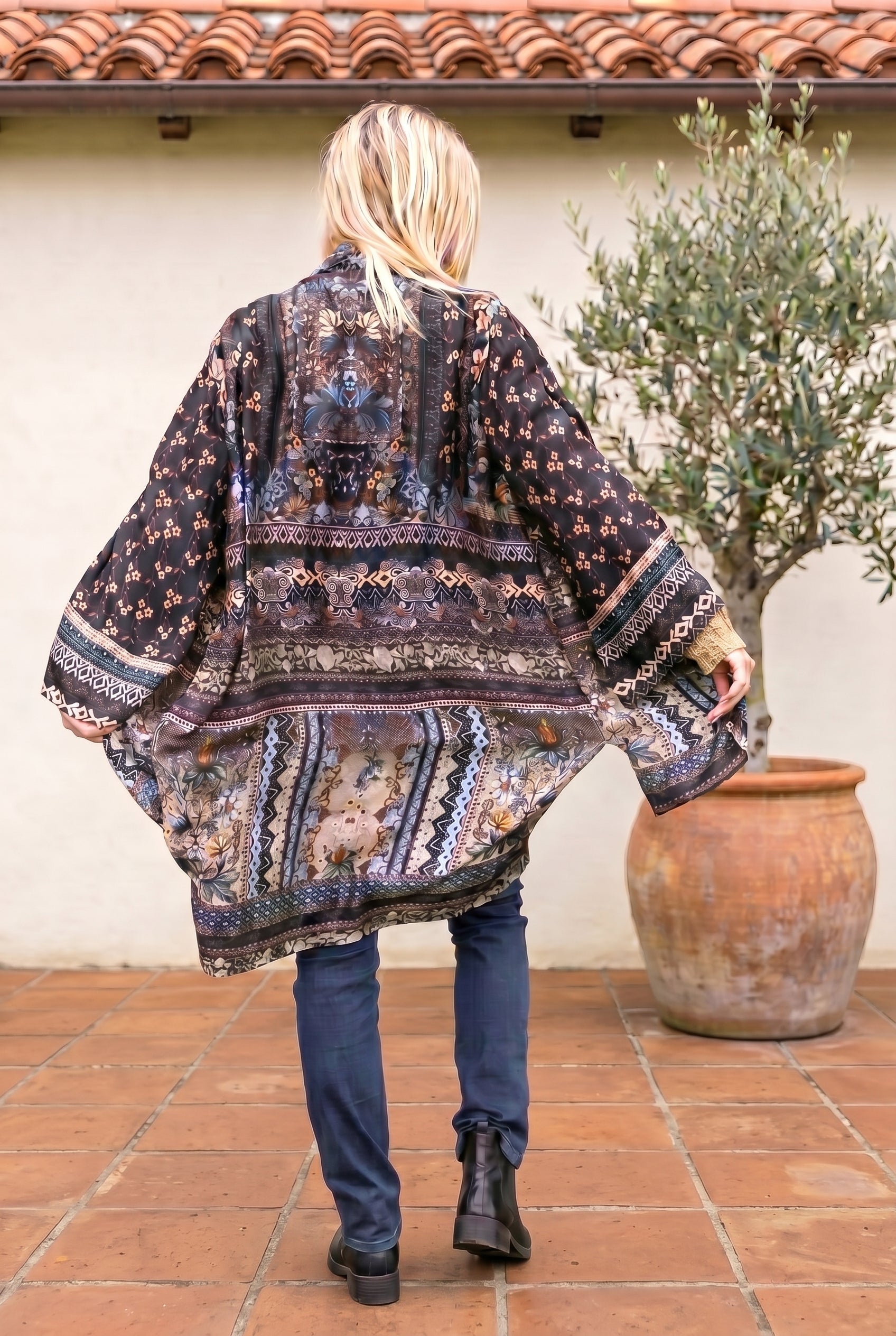 Person wearing a patterned kimono standing outdoors next to a potted plant.