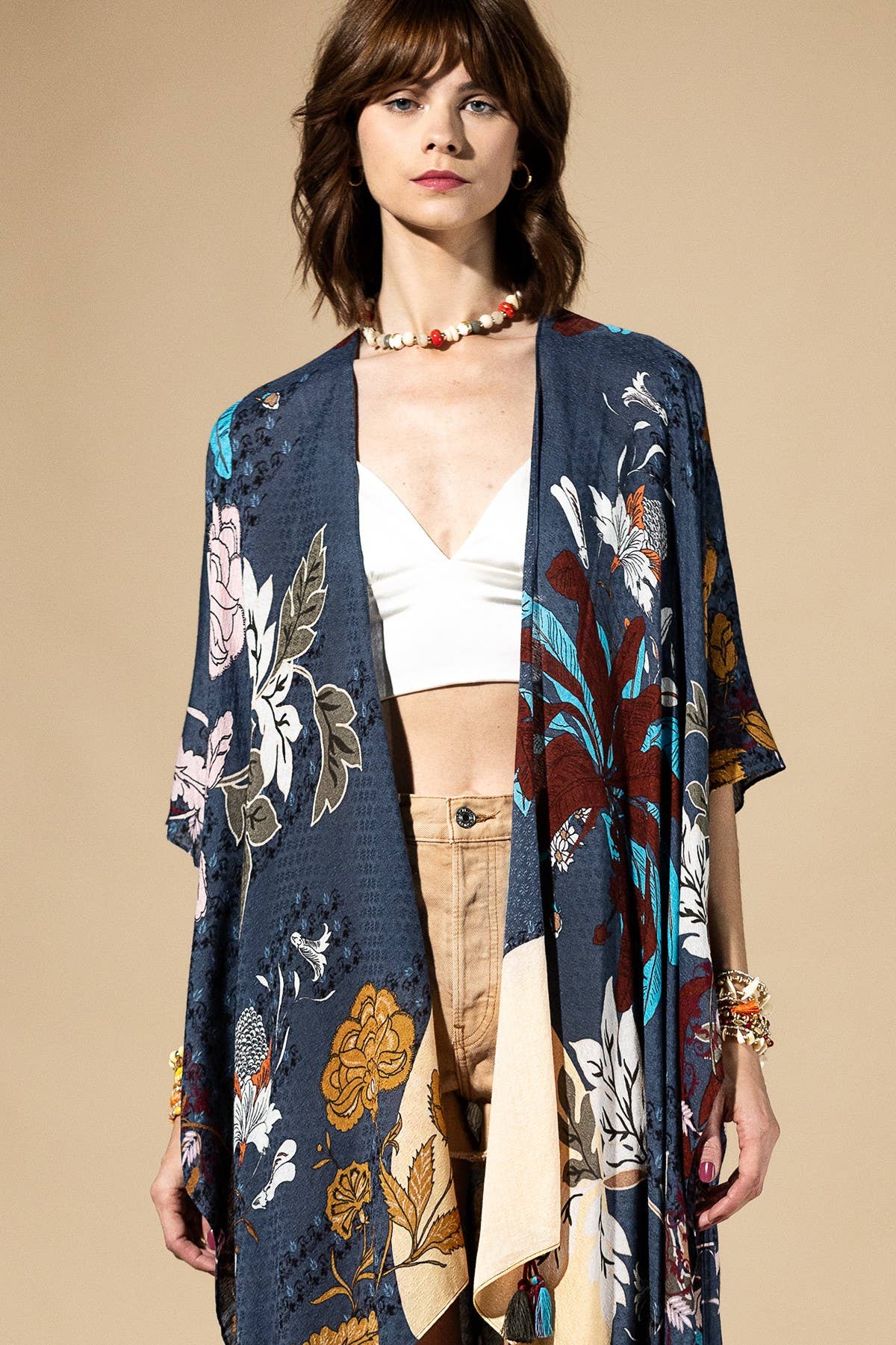 Woman wearing a floral kimono over a white top and beige pants on a beige background