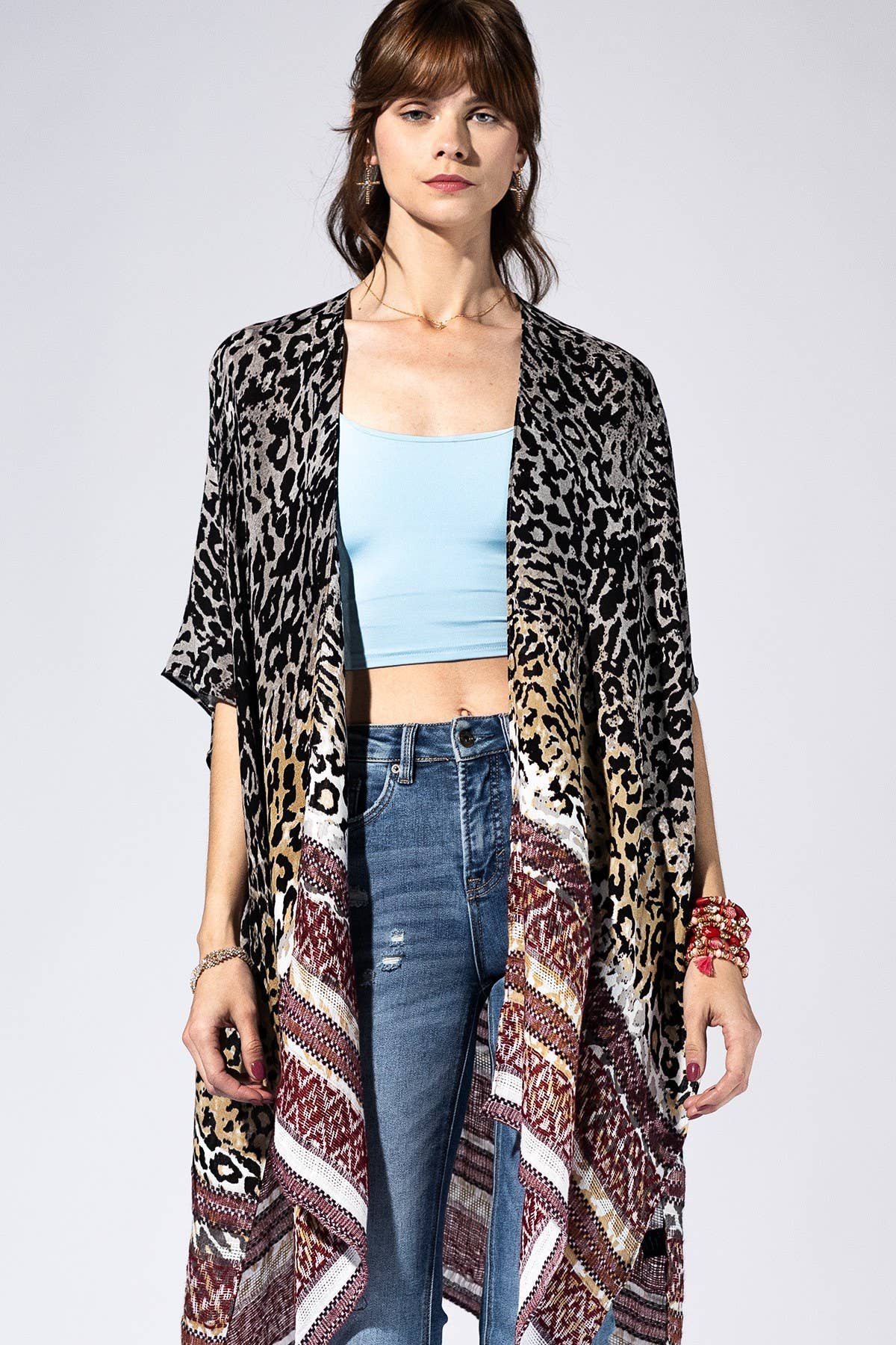 Woman wearing a leopard print kimono over a light blue top and jeans on a white background