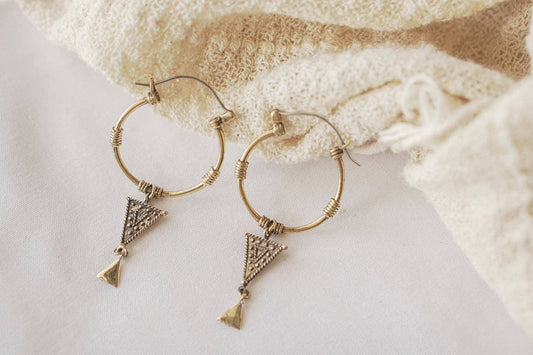 Gold hoop earrings with triangle-shaped charms on a textured white surface.