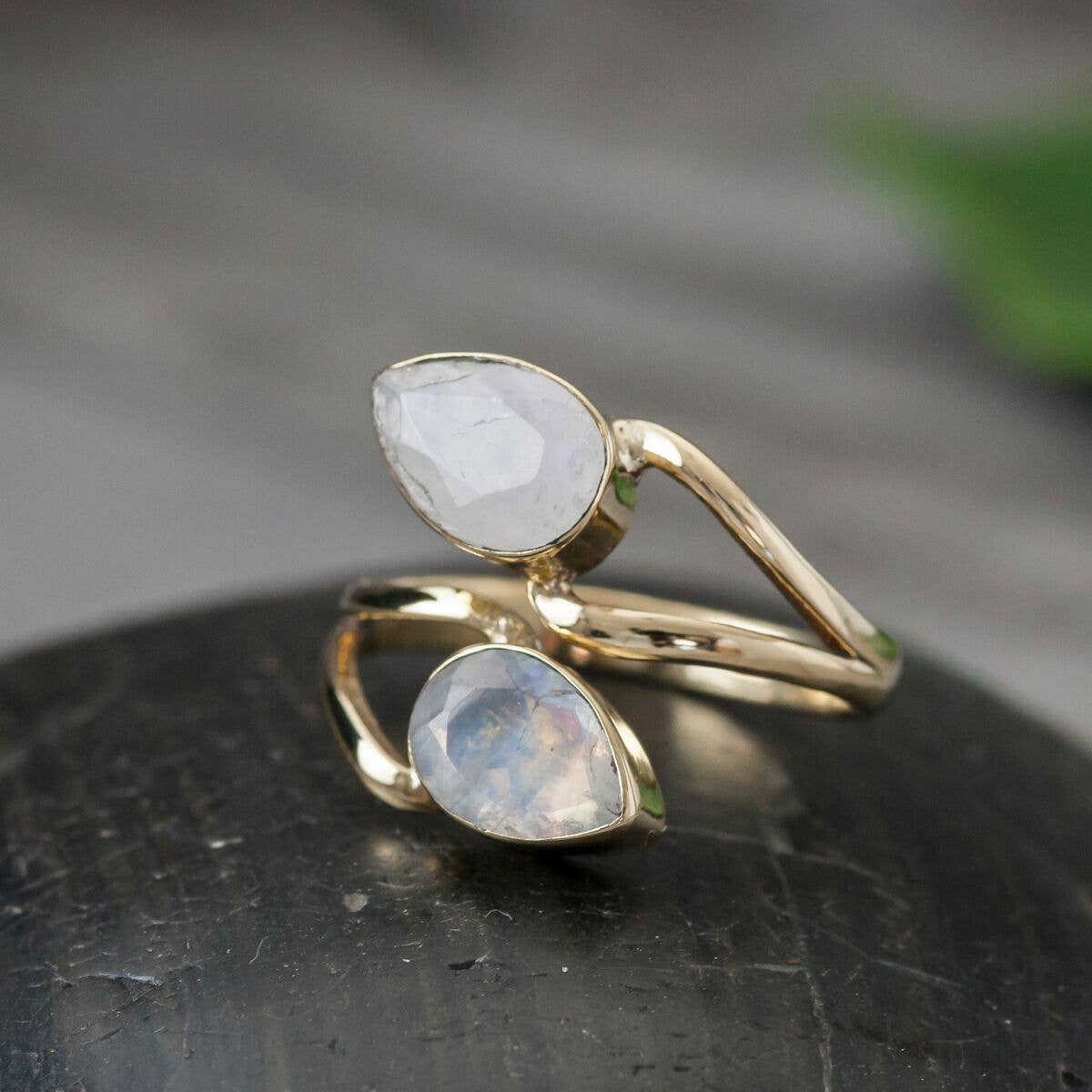 Two gold rings with teardrop-shaped gemstones on a dark surface.