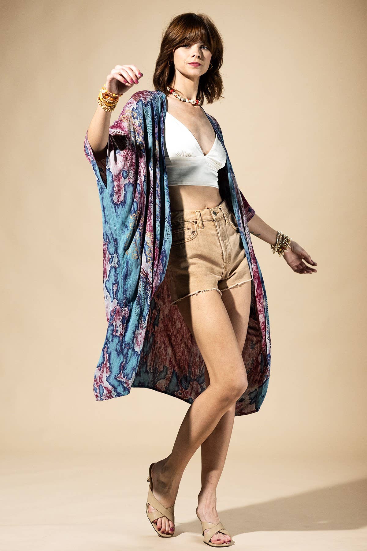 Woman wearing a colorful kimono over a white top and beige shorts on a beige background
