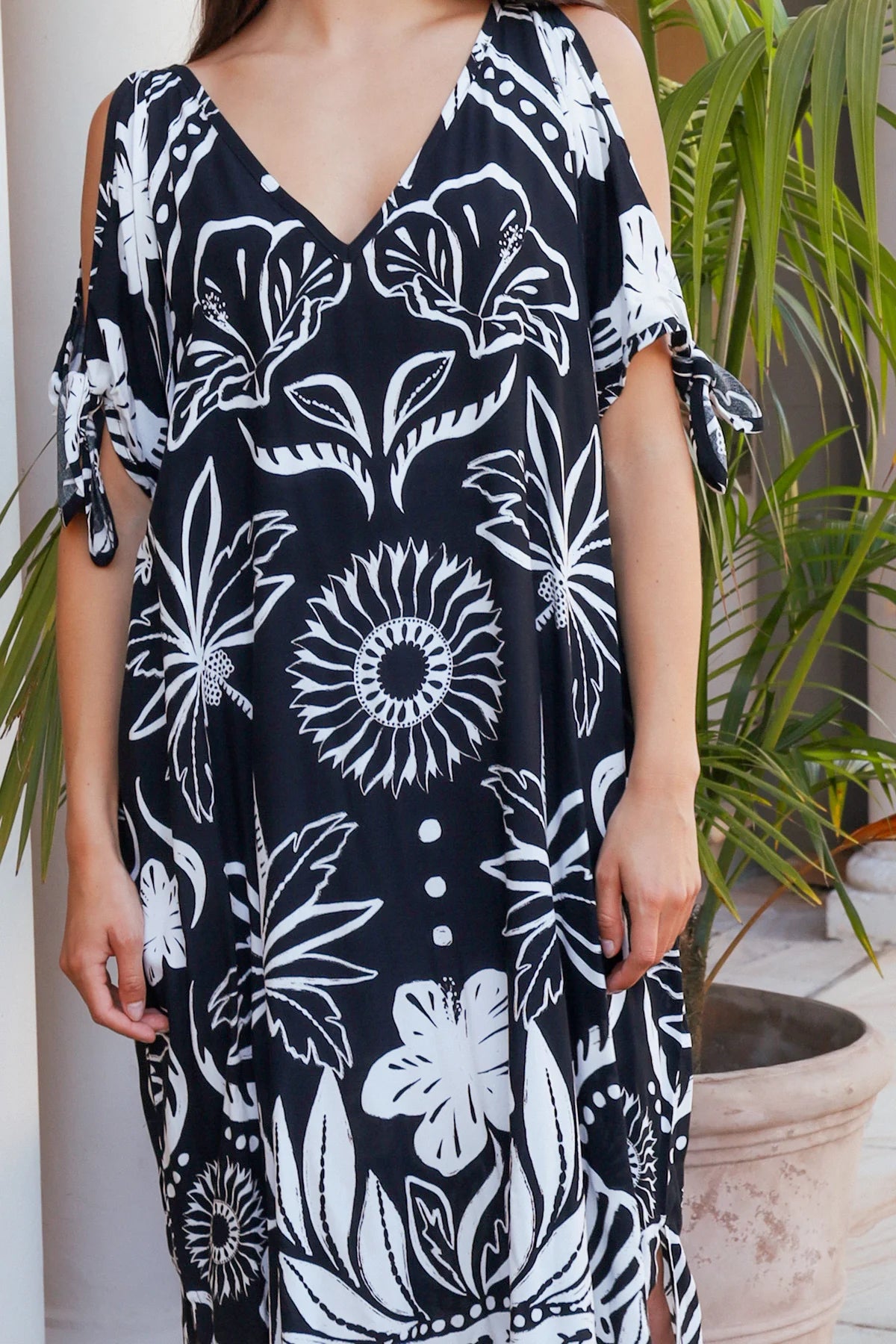 Woman wearing a black dress with white floral patterns, standing in front of plants.