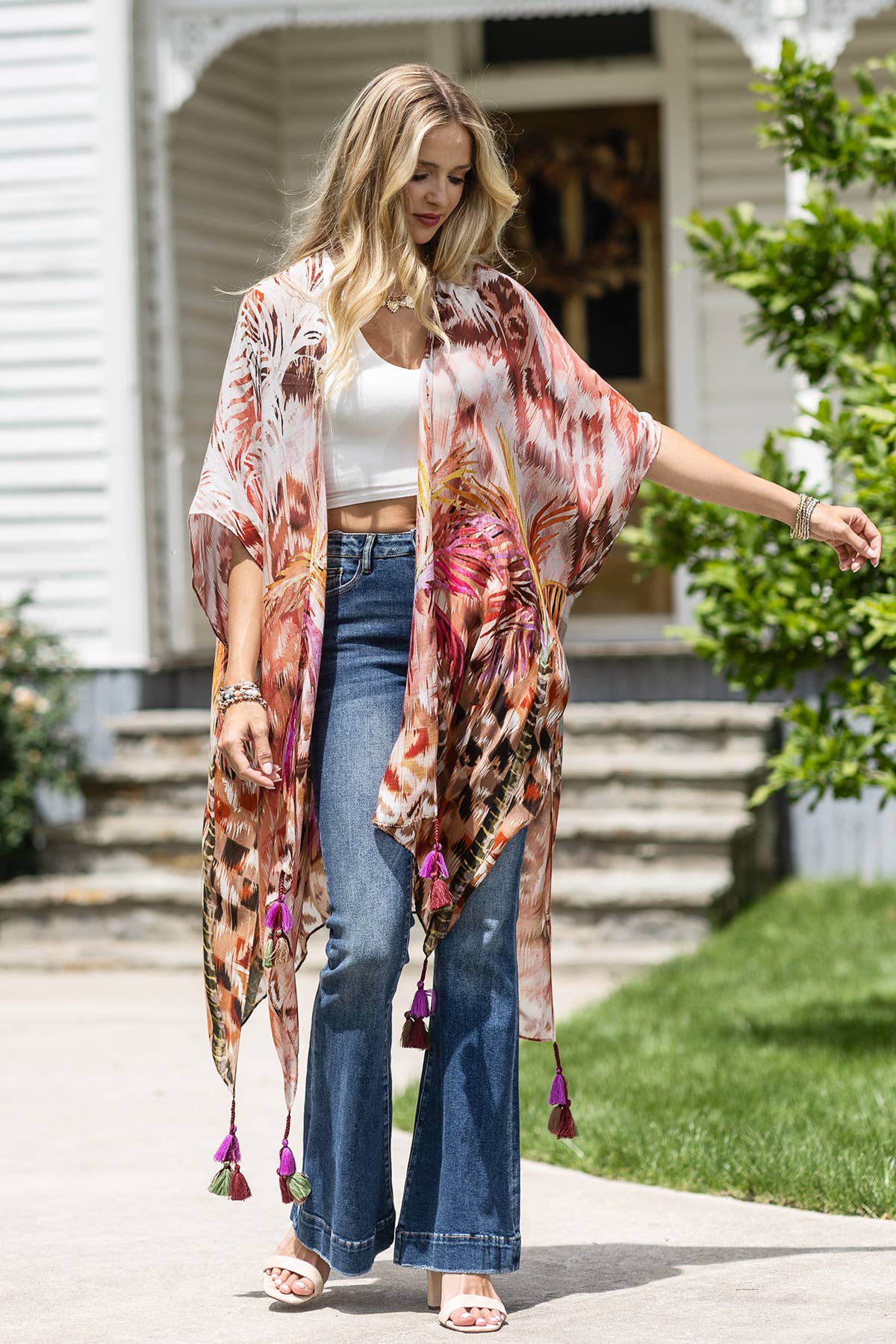 Woman wearing a floral kimono over a white top and blue jeans, standing on a sidewalk.