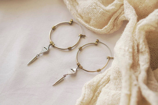 Gold hoop earrings with arrow-shaped charms on a light fabric background