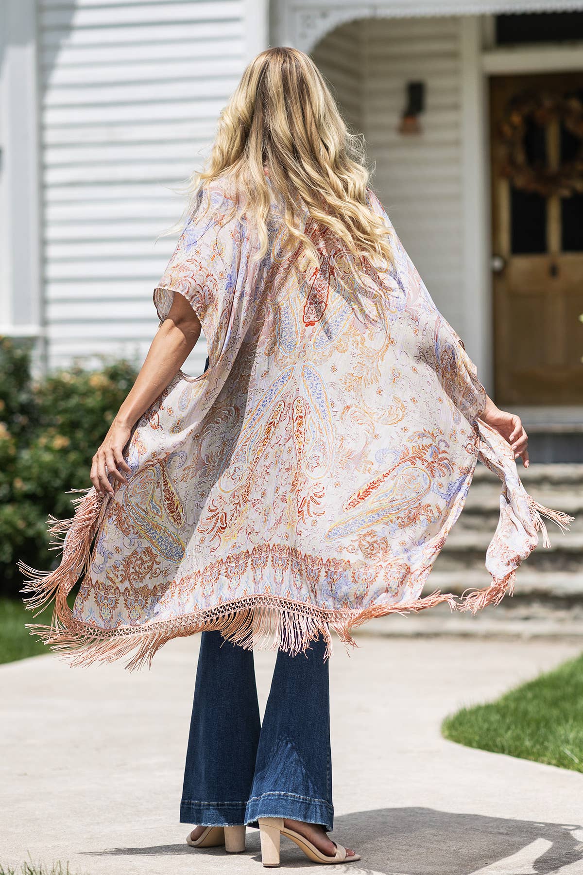 Woman wearing a patterned kimono-style garment with fringes outdoors.