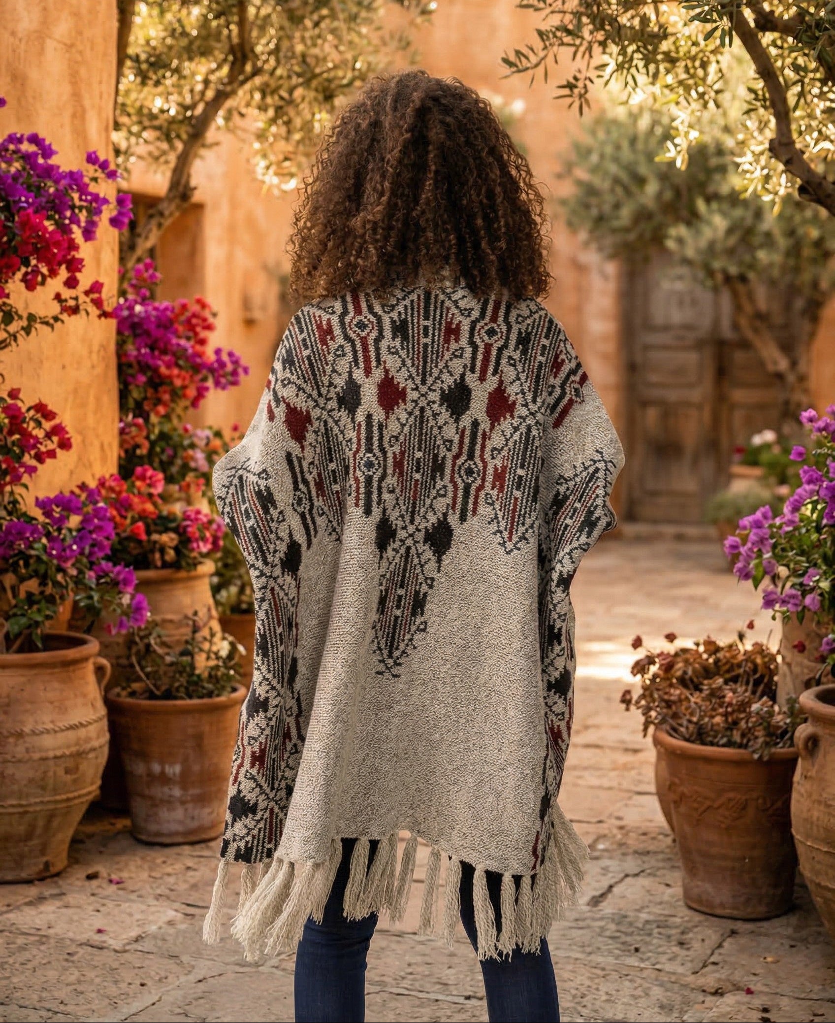 Person wearing a patterned poncho in a garden setting with potted plants and flowers.