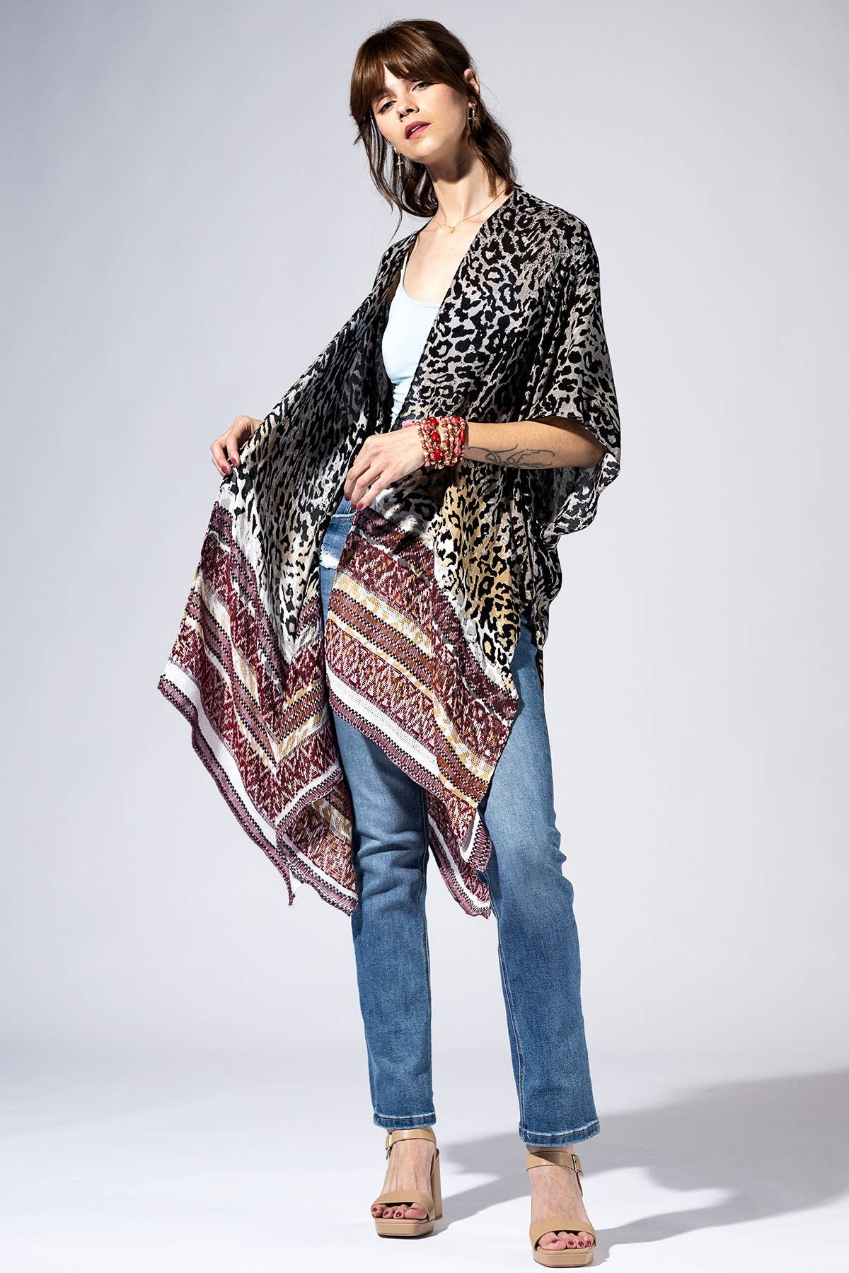 Woman wearing a patterned kimono over a white top and blue jeans on a white background