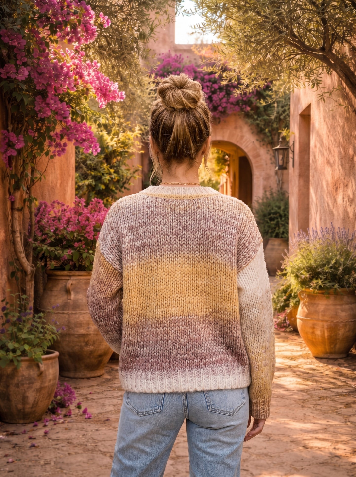 Person wearing a colorful sweater standing in a garden with flowers and arches.