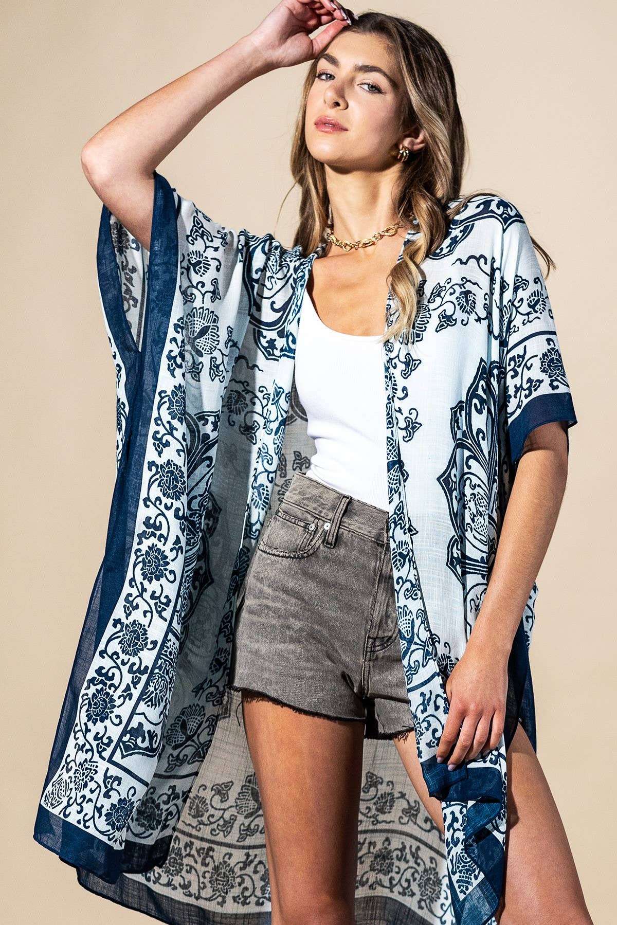 Woman wearing a blue and white patterned kimono over a white top and gray shorts on a beige background